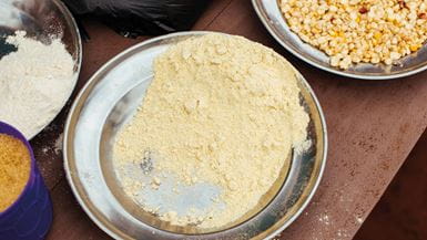 Pratos prateados no Burundi contendo grãos de milho amarelos e farinha de milho amarela