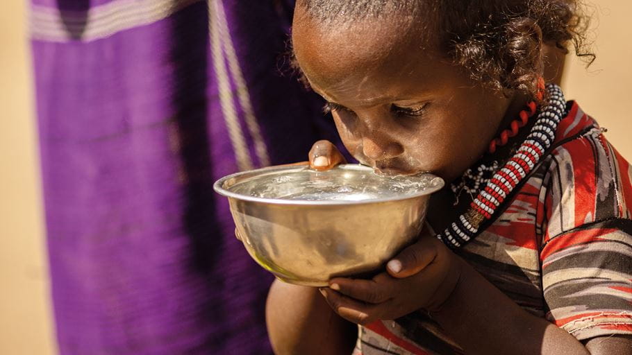 Um menino da Etiópia bebendo água de uma tigela prateada