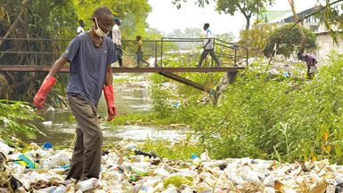 A man wearing red gloves stands on piles of plastic waste in the Kalamu River, Democratic Republic of Congo.