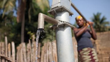 Water flows out of a metal handpump being used by a woman in Sierra Leone.