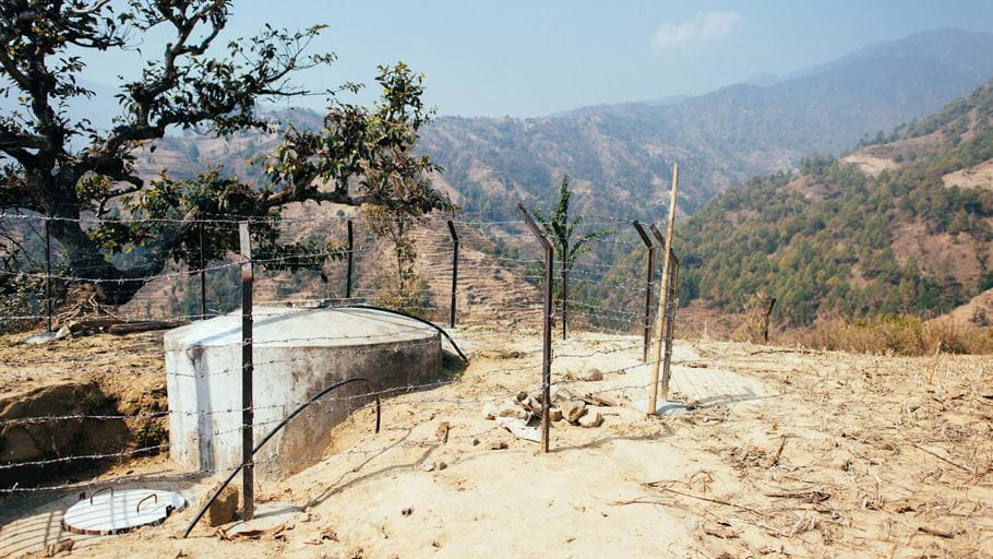 A covered, gravity-fed concrete water tank has a protective fence around it in Nepal.