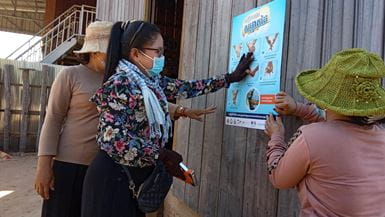 Three ladies putting up a poster about handwashing in Cambodia
