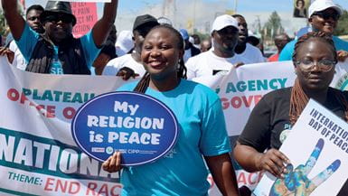 Nigerian women and men walk along an urban road carrying placards and banners with messages of peace