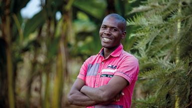 A young Burundian man in a pink t-shirt smiles at the camera