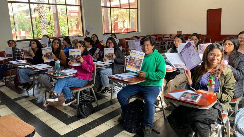 A group of seated university students in Peru hold up the copies of Footsteps magazine that they are reading