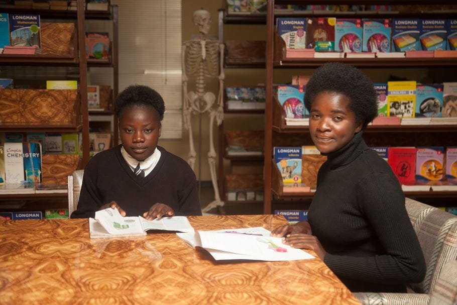 Two Zambian young women sit reading at a table inside a library.