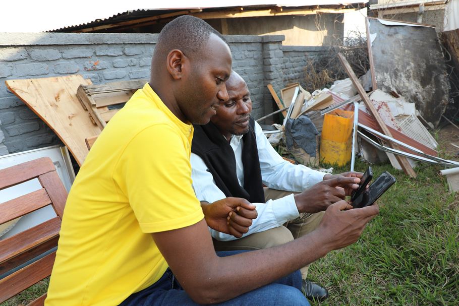 Dos hombres ruandeses se sientan al aire libre y miran las pantallas de sus smartphones.