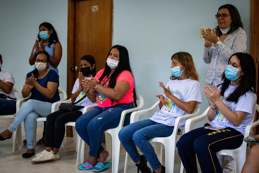 Um grupo de mulheres venezuelanas, muitas delas usando máscaras, batendo palmas dentro de um prédio na Colômbia.