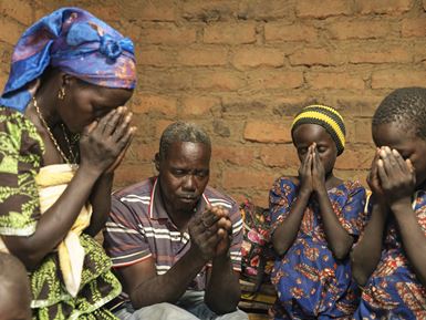 A family of four in Chad pray with their hands close to their faces, next to a brick wall.