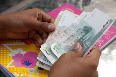 The hands of a person in Cambodia hold bank notes of different sizes and colours.