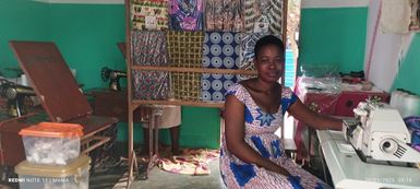 A woman in Togo sits next to her sewing machine inside her tailoring shop.