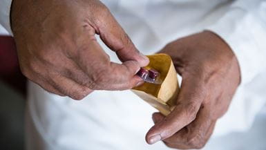 Un hombre que usa una capa de laboratorio blanca saca dos píldoras de medicamentos de una pequeña bolsa de papel marrón.