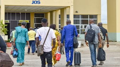 Un groupe d'hommes et de femmes transportant des valises, marchez vers l'entrée de l'aéroport de Yakuba Gowon à Jos, au Nigéria,