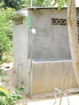 Récupération des eaux de pluie de la toiture d’une latrine au Cambodge, à l’aide d’une bouteille usagée de boisson gazeuse, un tuyau en plastique dur, une tôle ondulée et une citerne de stockage en brique. Ce concept est particulièrement utile car il fournit de l’eau pour se laver les mains directement à la porte de la latrine. Photo : Murray Burt/Tearfund