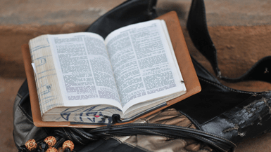 An open Bible sits on top of a leather bag 