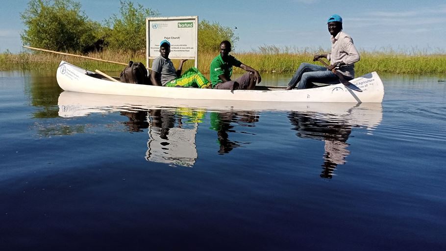 Three African men in a canoe in a flooded area of South Sudan