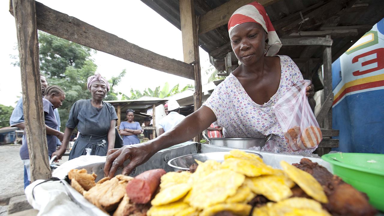 Uma mulher de negócios vende lanches quentes em sua banca de mercado no Haiti. Foto: Warren Allott/Tearfund