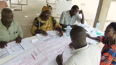 Un grupo de colaboradores de Tearfund en Chad, formado por dos mujeres y tres hombres, trabajan juntos alrededor de una mesa para fortalecer las capacidades en sus comunidades