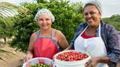 Deux femmes du nord-est du Brésil sourient et tiennent des seaux de fruits frais, dont des mini-pommes vertes et rouges.