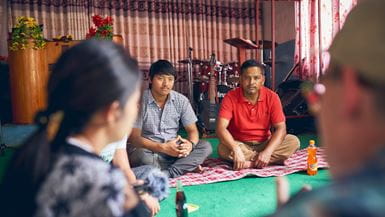 Deux membres d’une église au Népal, portant des chemises à col, sont assis sur le sol de l’église et discutent du travail communautaire.