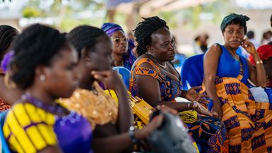 Cuatro mujeres de Diégonefla, en Costa de Marfil, con vestidos tradicionales de color azul y amarillo y sentadas una al lado de la otra, sonríen y hablan sobre cómo movilizar a la iglesia local