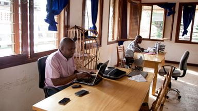 Dos empleados de Tearfund, sentados en sus escritorios en la oficina de Bangui (República Centroafricana), miran la pantalla de sus computadores portátiles