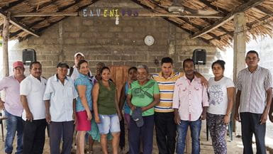 Membros de uma comunidade no norte da Colômbia em uma igreja com telhado de palha, lado a lado, com os braços em volta uns dos outros