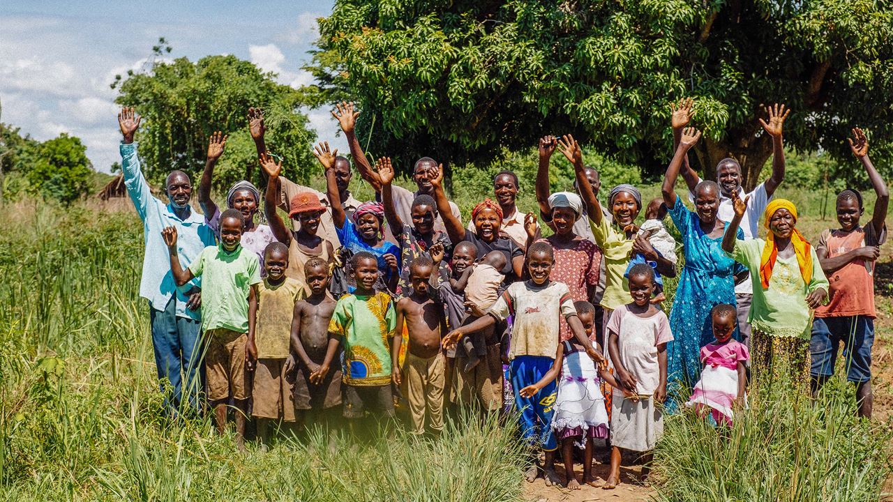 Community members smiling and waving to camera in Uganda, Africa.