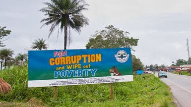 Uma placa azul na estrada em Freetown, na Serra Leoa, dizendo “Fight corruption and wipe out poverty” (combata a corrupção e acabe com a pobreza, em inglês)