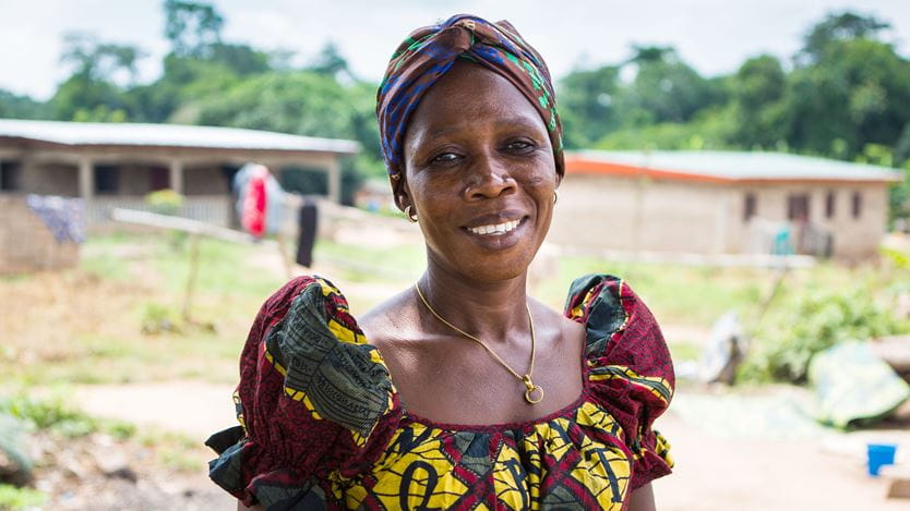 Uma mulher africana sorridente usando um vestido colorido e um adereço de cabeça combinando. N'Govie Amenan Adele, membro da igreja CCMP, Manglai-kan, Costa do Marfim.