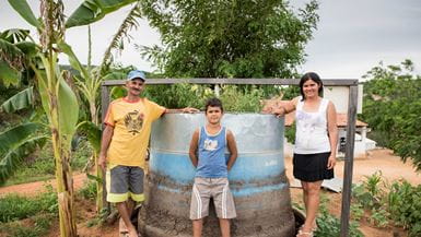 Uma família de agricultores, composta por um homem, uma mulher e seu filho, posando para a foto com seu grande biodigestor